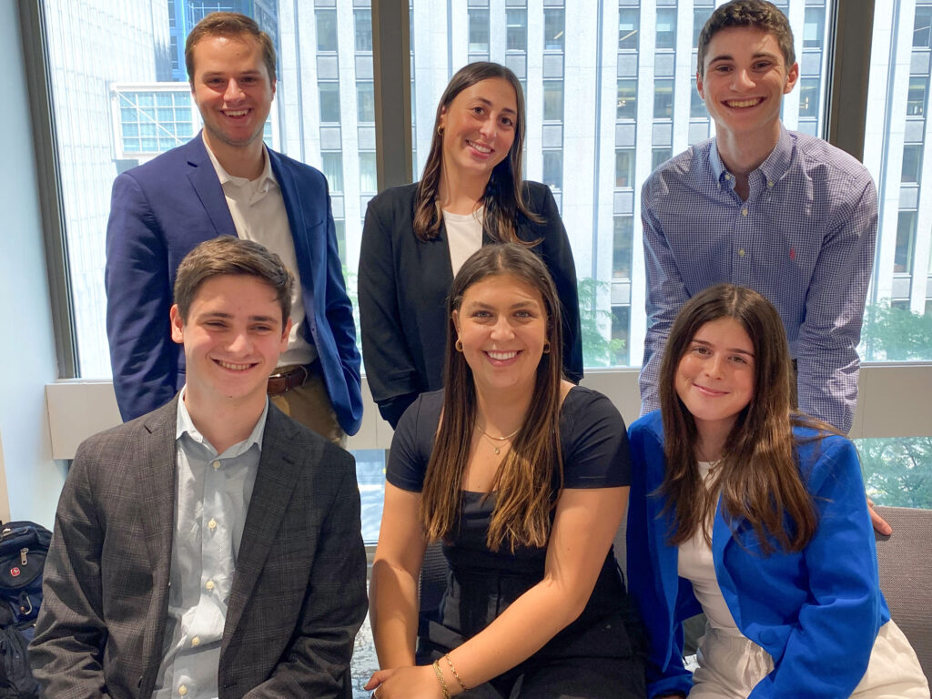 Two rows of three college students each sitting and standing in business clothes smiling.