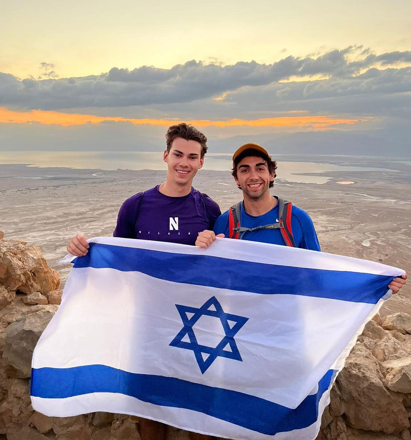Two college aged men at the top of Masada in Israel holding the Israeli flag.