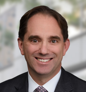 Executive Director of Public Affairs Dan Goldwin headshot smiling with black suit and polka dot pink tie.