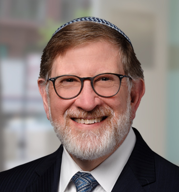 VP of HR Louis Lazovsky head shot smiling wearing round glasses, a blue kippah and blue tie with a black suit.
