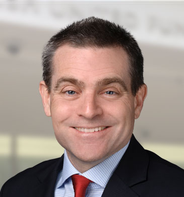 Headshot of CEO Lonnie Nasatir wearing a black suit and red tie smiling.