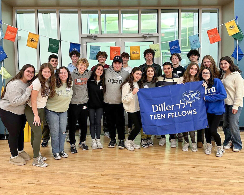 A group of Diller Teens posing in two rows for a photo with a blue flag reading "Diller Teen Fellows".