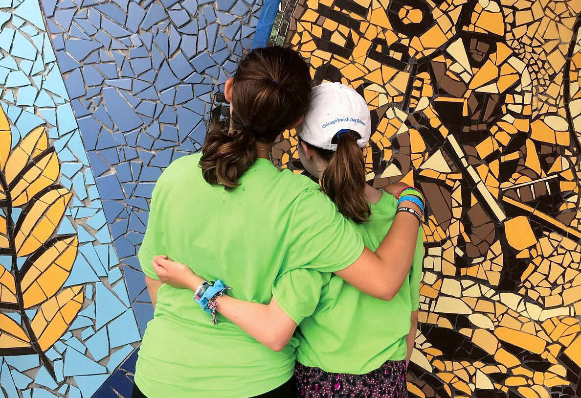 Two teen girls wearing neon green t shirts hugging while facing the peace wall in Israel.