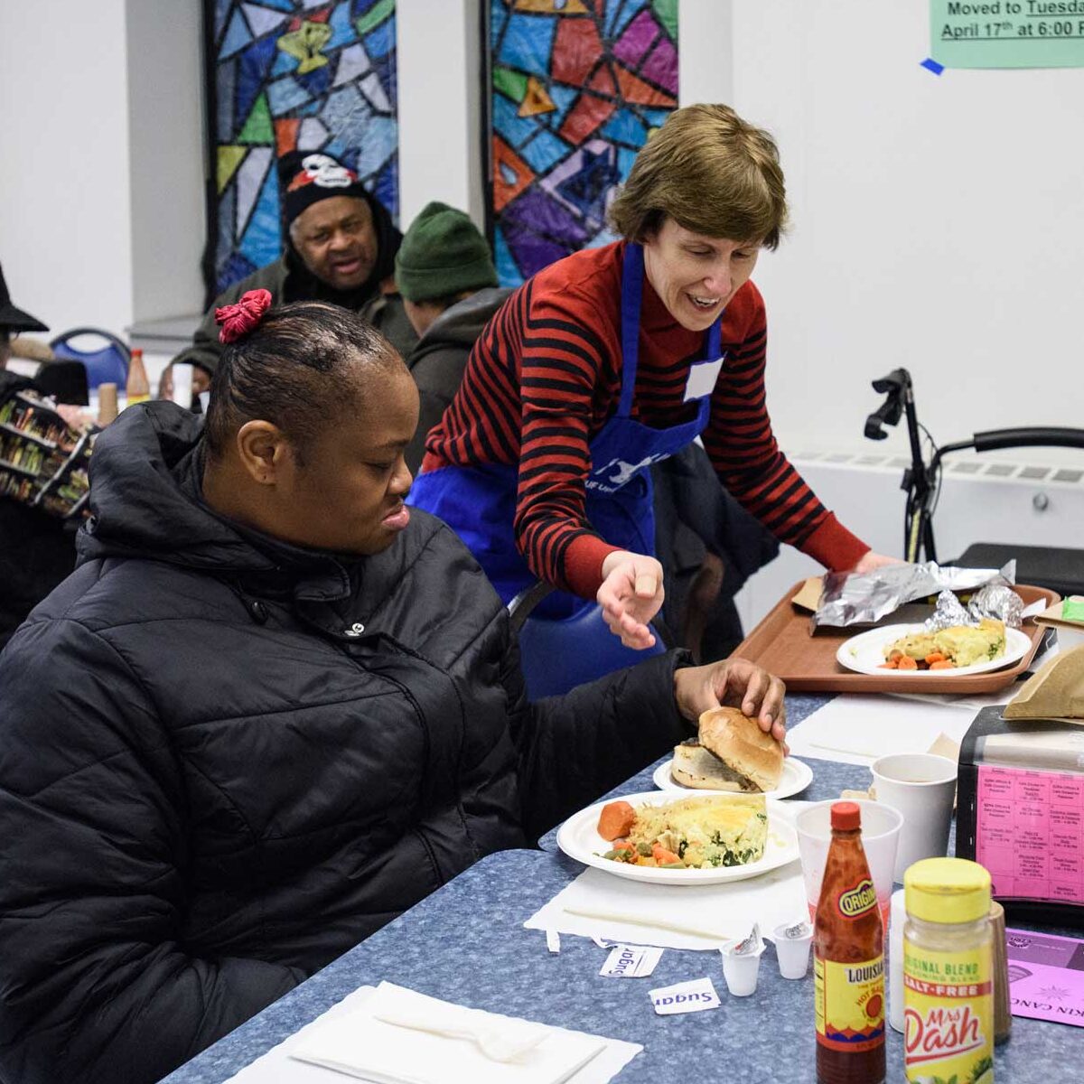 A JUF Uptown cafe female volunteer serving a client at the table.