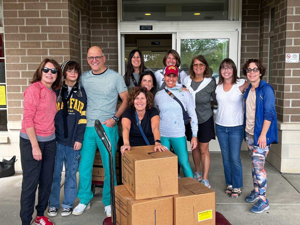 A group of women and one man in front of a cart with large brown cardboard boxes volunteering.