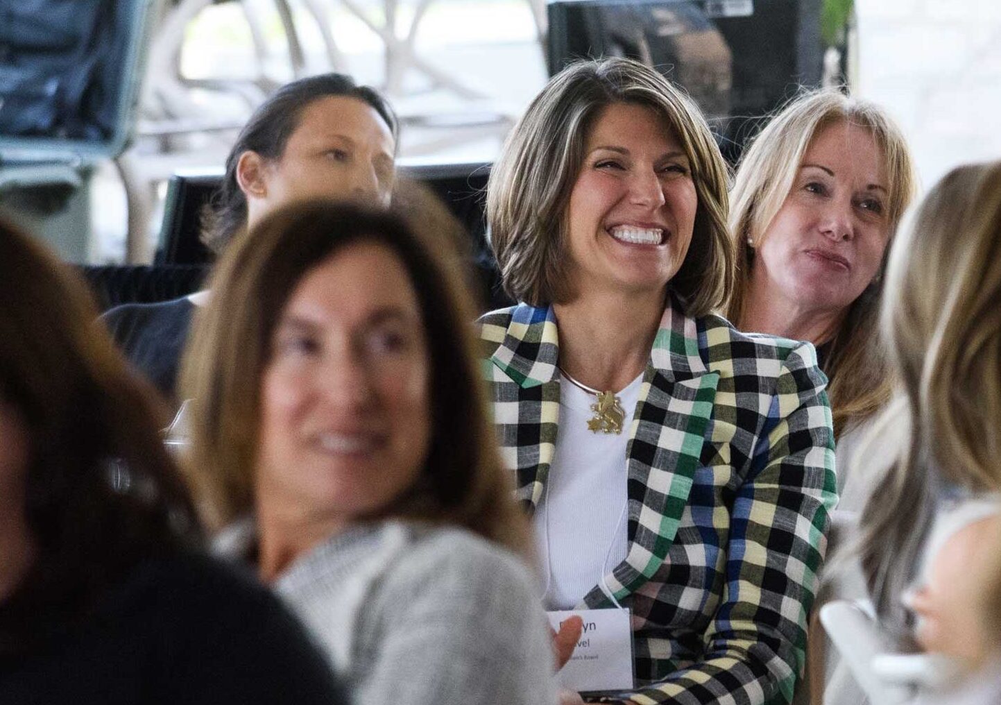 A woman sitting and smiling at a women's event wearing a name tag and a "Lion of Judah" necklace.