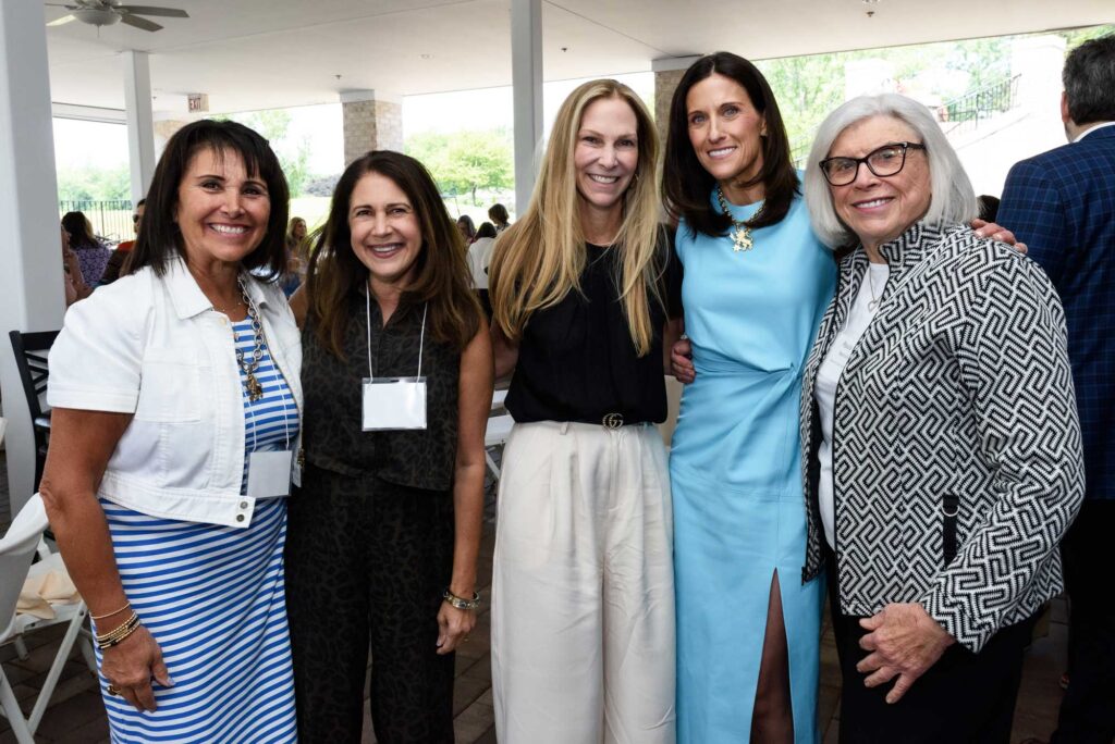 A group of five women wearing business professional clothes smiling for the photo.