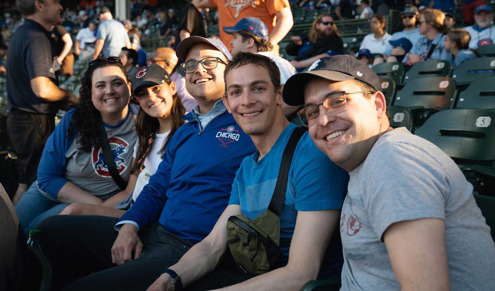 A group of five individuals sitting in stadium seating at Wrigley Field, watching a Chicago Cubs game.
