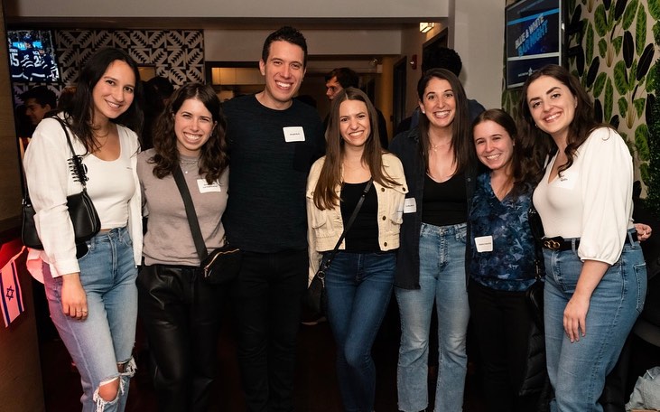 A group of Jewish young adults standing with arms around each other each wearing name tags including six women and one man.