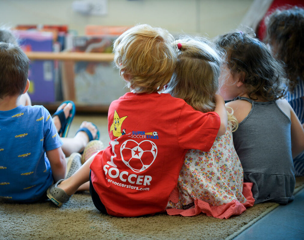 A group of toddlers sitting on a carpet hugging.