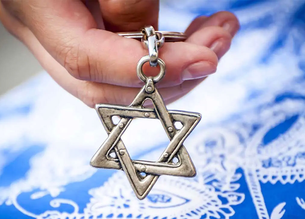 A closeup hand holding a silver magen david.