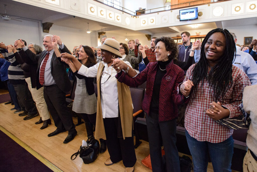 A group of diverse individuals holding hands and smiling in a place of worship.