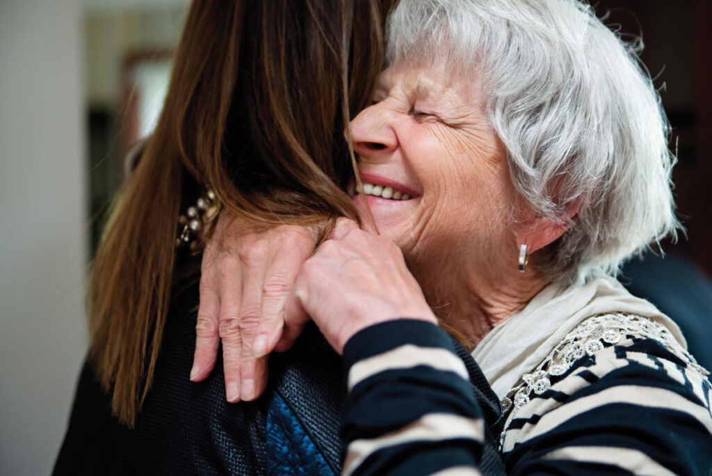 Two women hugging tightly, close-up of older woman smiling with eyes closed.