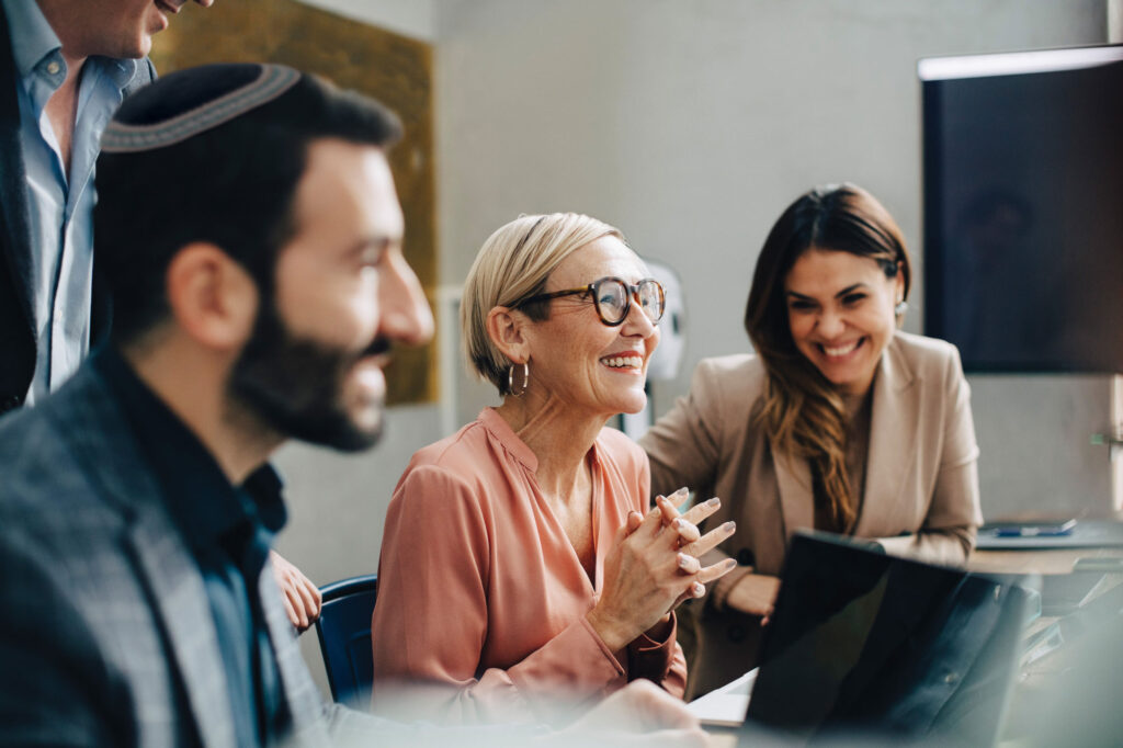 One man wearing a kippah and two women dressed in professional clothes sitting at a conference table smiling.