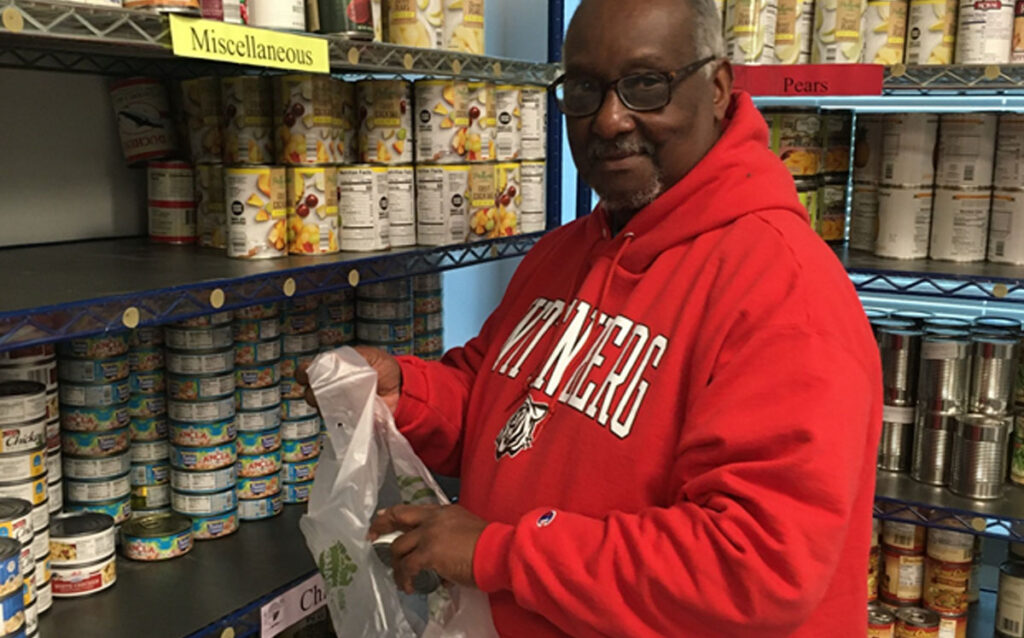 A man in glasses and a red sweatshirt packing canned foods in the food pantry.