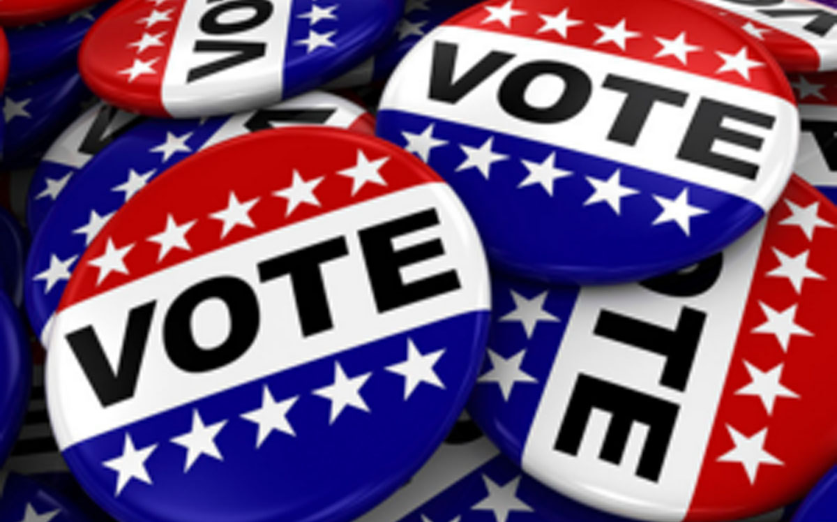 A pile of red, white and blue pins that say "VOTE" on them with white stars.