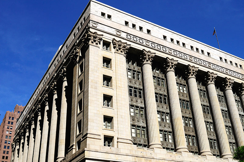 The corner of Chicago City Hall featuring bright blue sky and cream colored pillars.