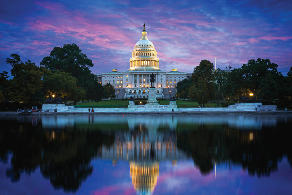 The capitol in Washington DC in the evening with purple clouds behind and reflection in the body of water in front of the building.
