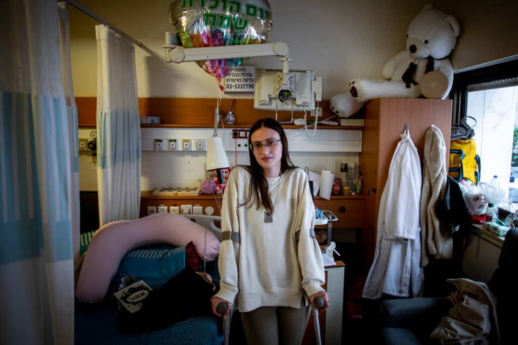 A female October 7 survivor standing with canes in her recovery hospital room.