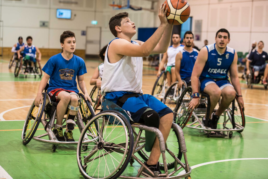 A group of high school boys playing basketball in a gym all in wheelchairs wearing blue and white for Israel.