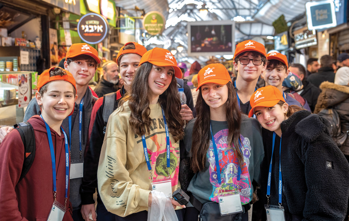 A group of teens wearing orange "Israel Now" hats and name tags at the shuk in Jerusalem.