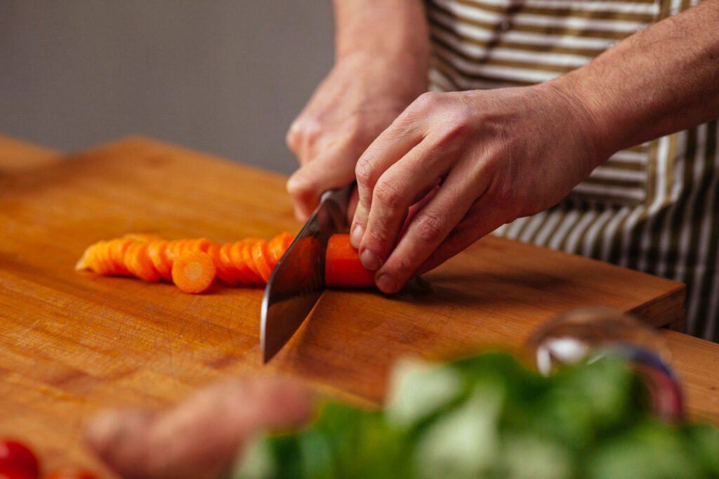 A close up photo of a woman chopping up a long orange carrot.