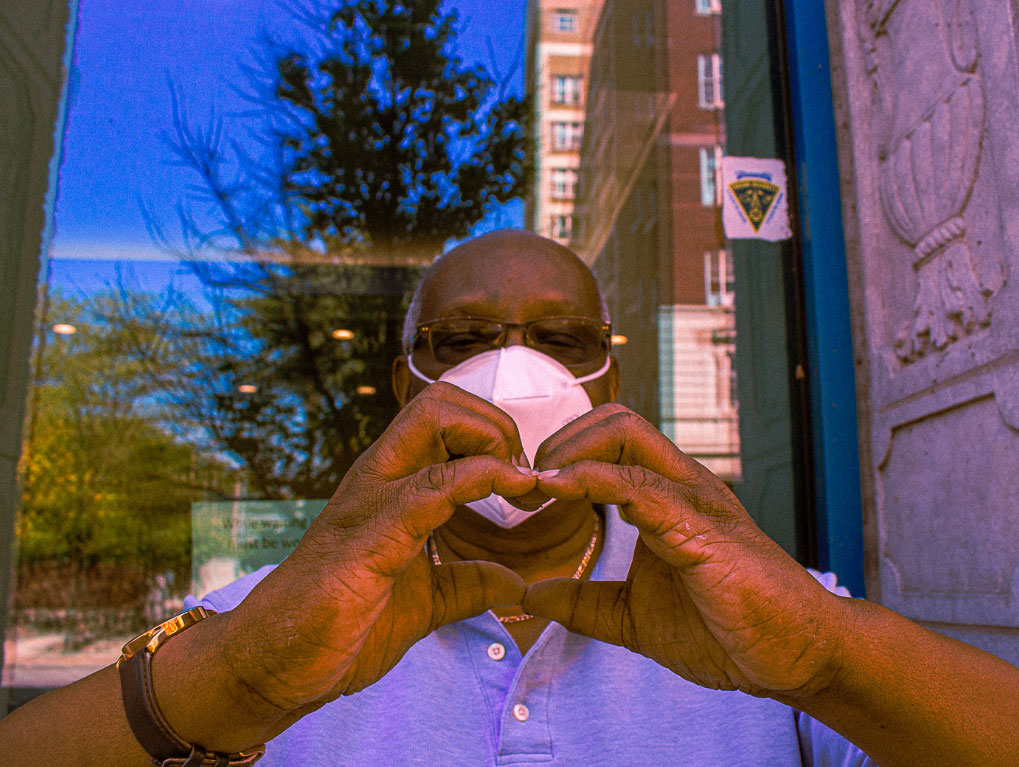 A man wearing a mask and glasses while making a heart with his hands.