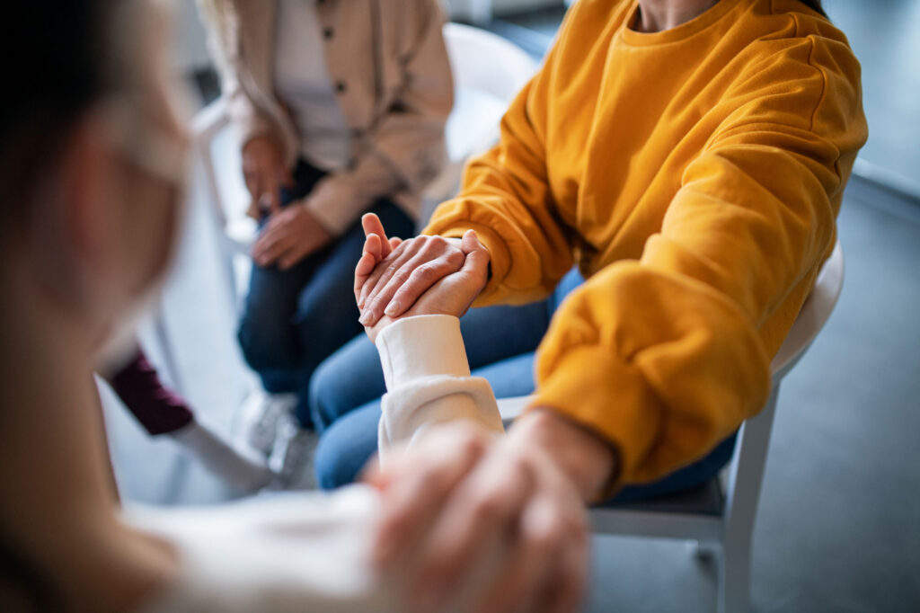 A close up of two people holding hands one in a bright yellow crewneck.