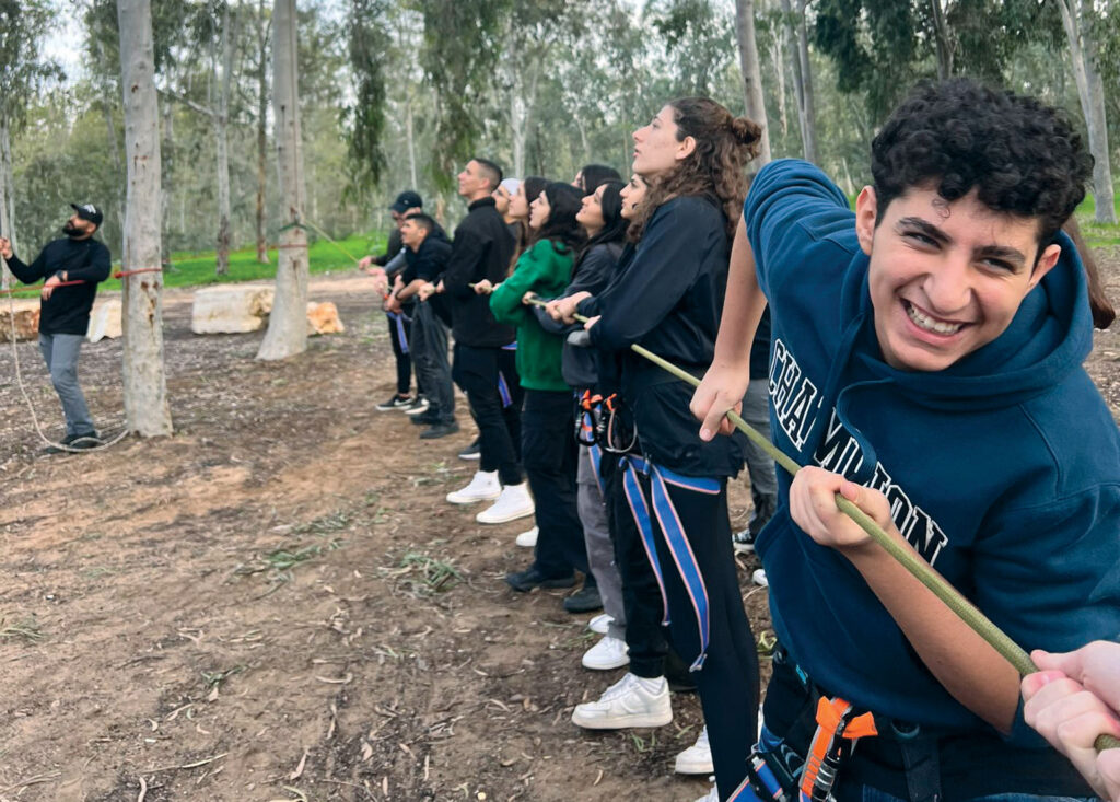A bunch of young people in a line all holding a rope doing a team building exercise.
