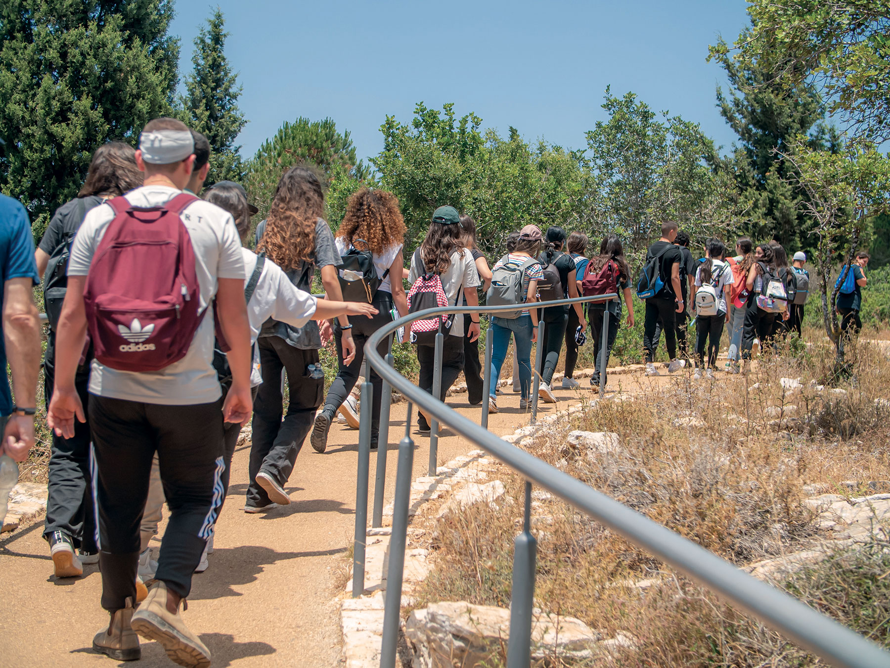 A tour group of people walking on a dirt path with backpacks alongside a railing.