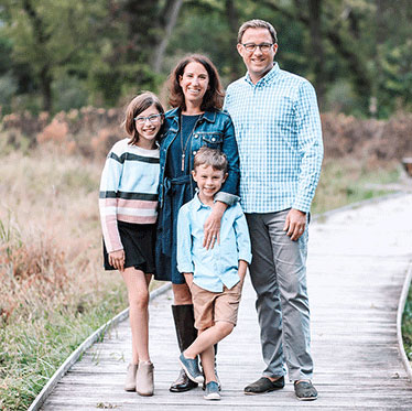 Michelle Farra and her husband standing on a wooden path with their elementary school-aged daughter and son all smiling for a portrait.