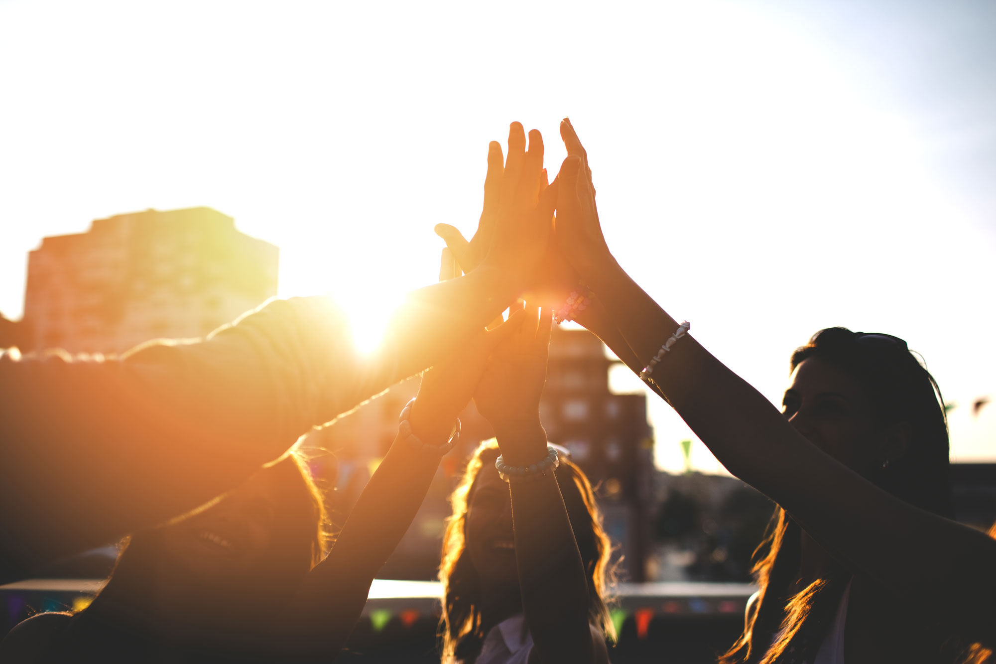 Sun shine rays coming through four people's hands as they go for a group high five.