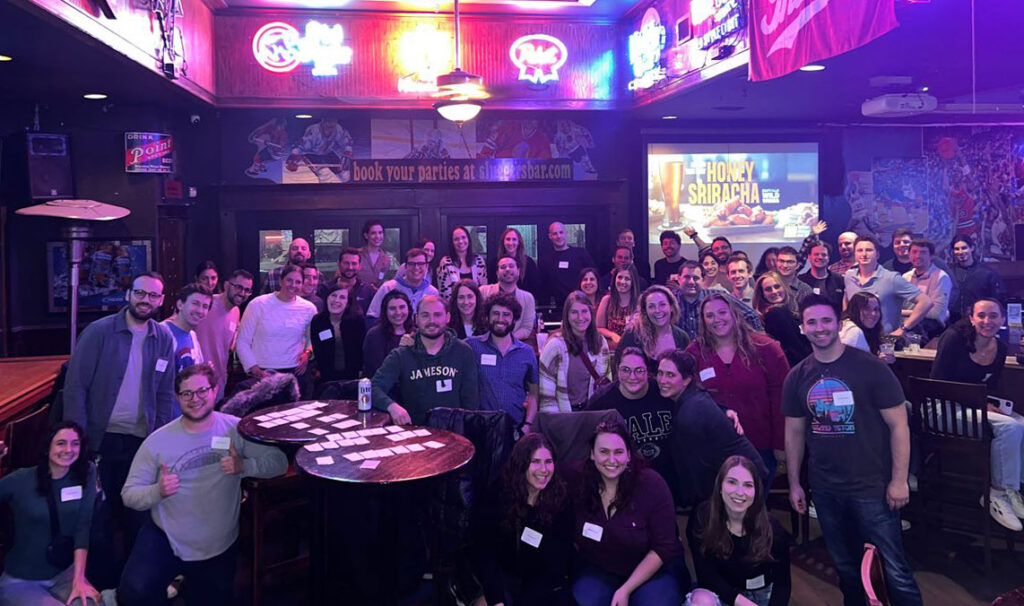 A large group of Jewish young adults posed smiling in a bar for a group photo all wearing name tags.