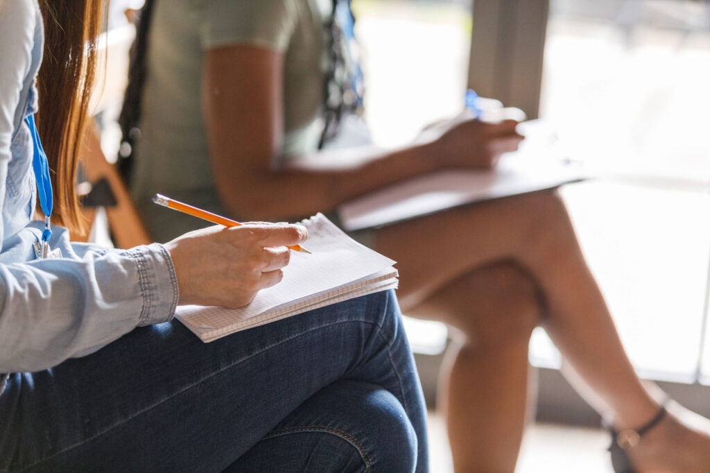 Two people sitting cross legged with a pencil and paper taking notes.