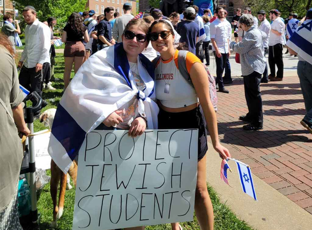 Two female college students holding a poster reading "protect Jewish students"