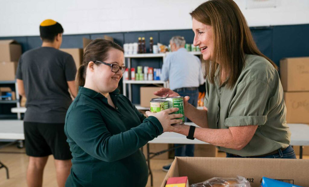 Two women passing canned food to each other to pack food boxes for people in need.