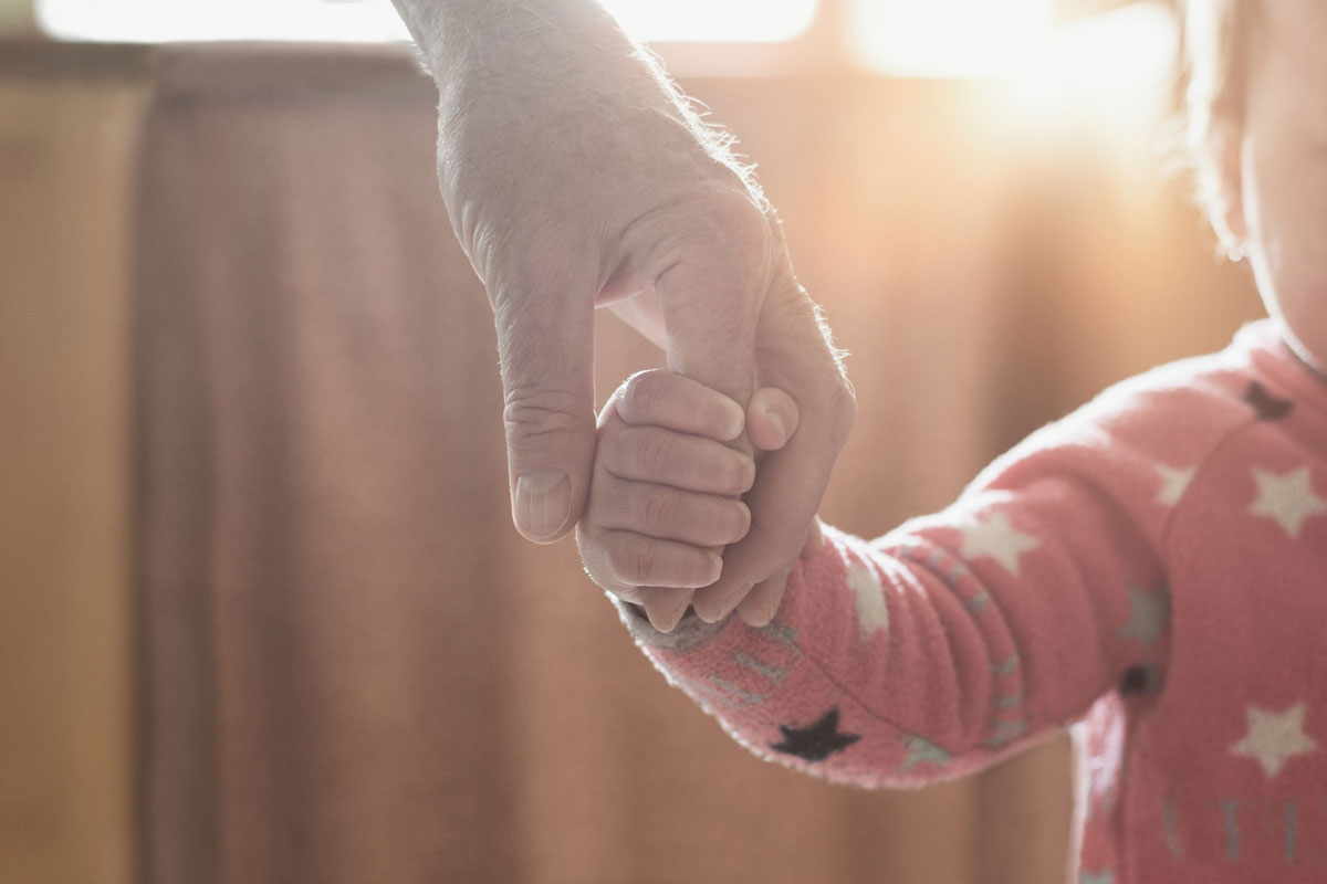 A close up of an adult holding a child's hand with sunlight shining through.