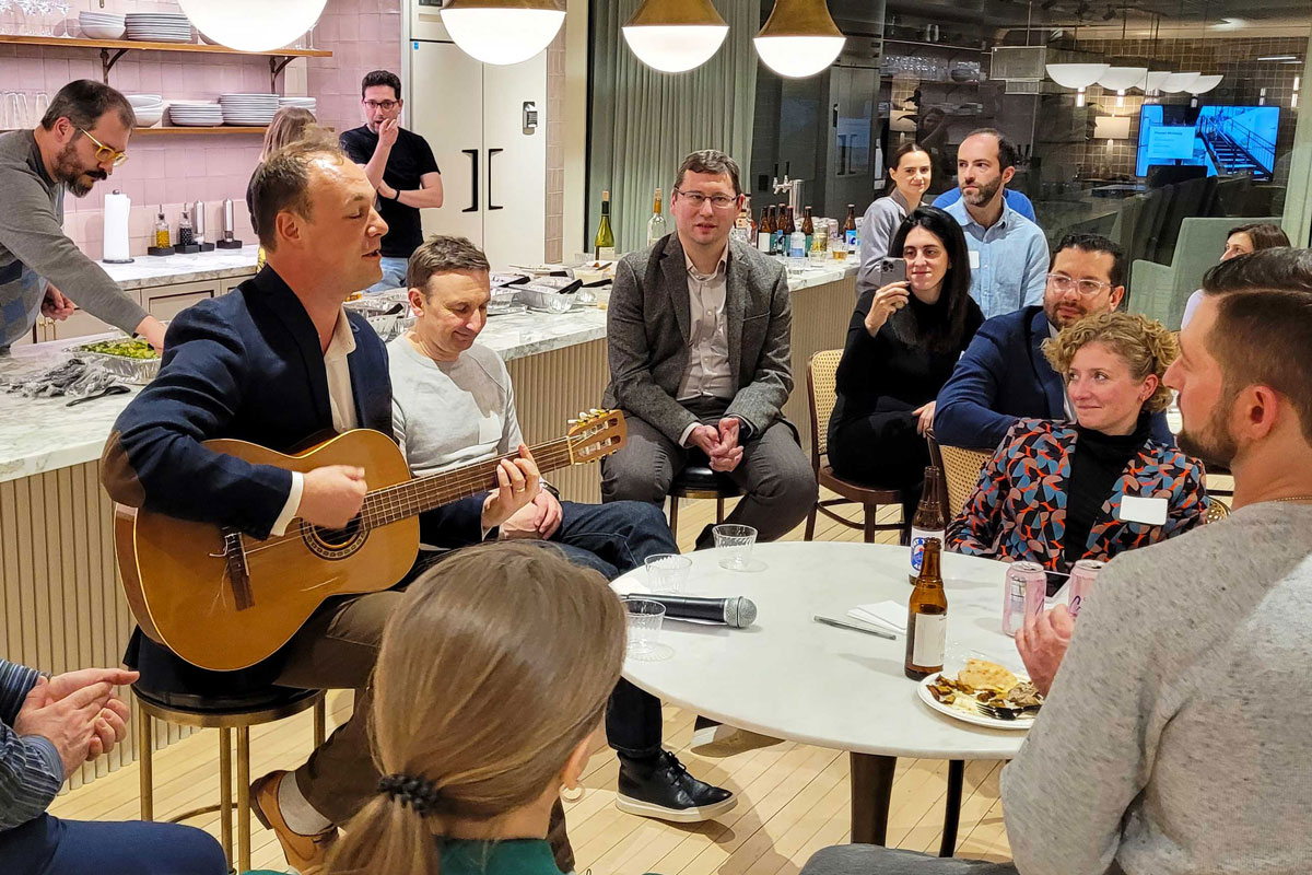 A man in a suit playing guitar for a crowd of people in a cafe.