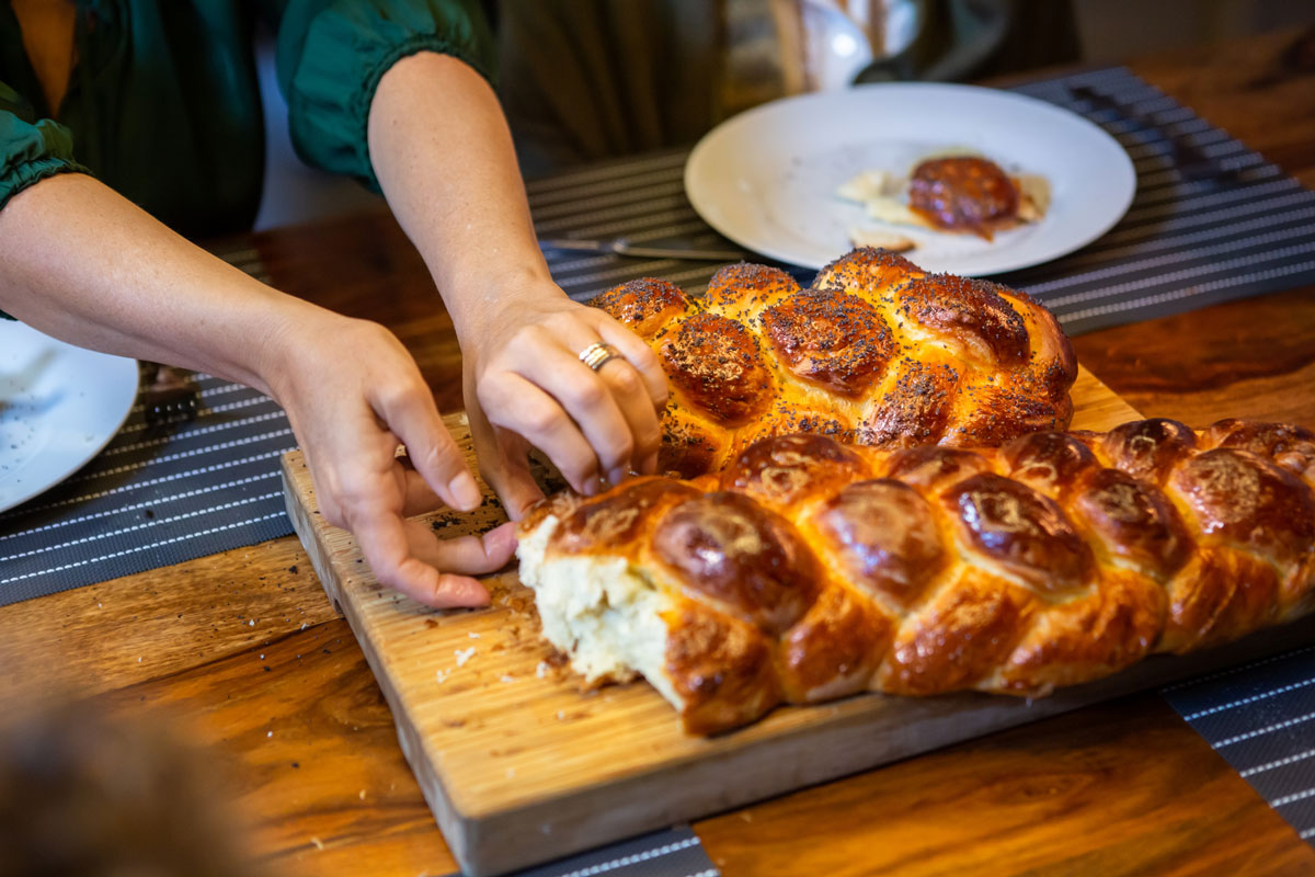 Two challah loaves on a challah plate being blessed with two hands.