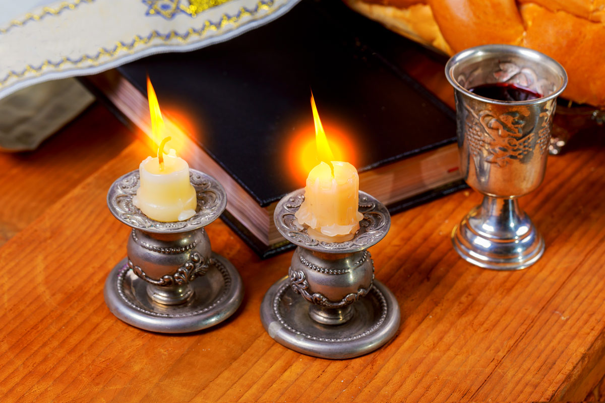 Two shabbat candles, one prayer book and one kiddush cup on display.
