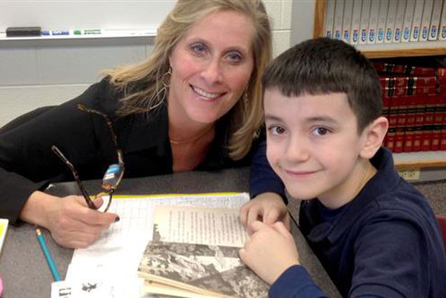 An older woman sitting with a boy tutoring him with a book open at a table.