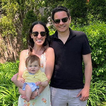 Jamie Yates and her husband standing in front of greenery wearing sunglasses while holding their baby.