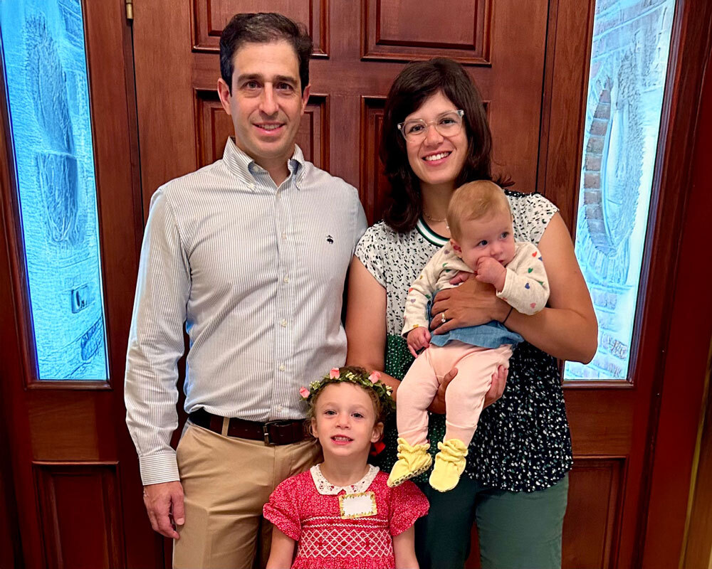 Nicole Beckmann Tessel and her husband holding their baby alongside their toddler girl standing in front of their front door of their house.