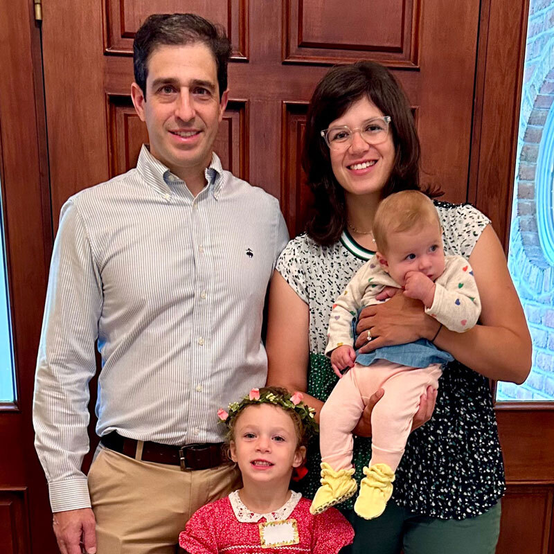 Nicole Beckmann Tessel and her husband holding their baby alongside their toddler girl standing in front of their front door of their house.