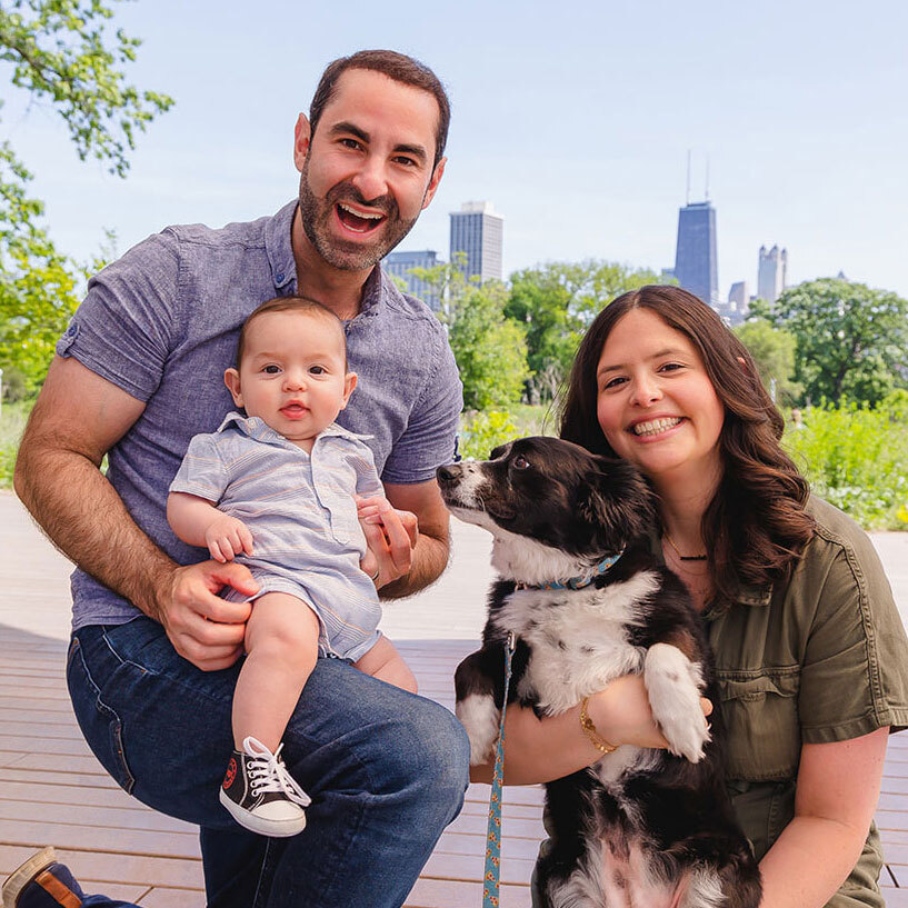 Leah Frydman with her husband, baby and dog in front of the Chicago skyline.