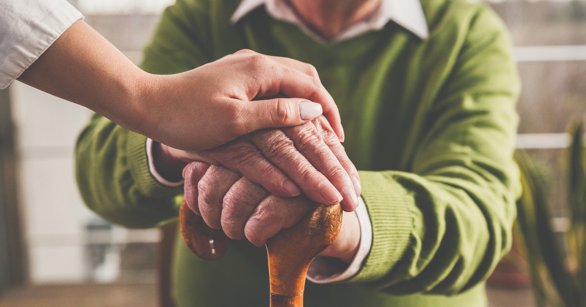 Hands of a nurse and senior man on walking cane