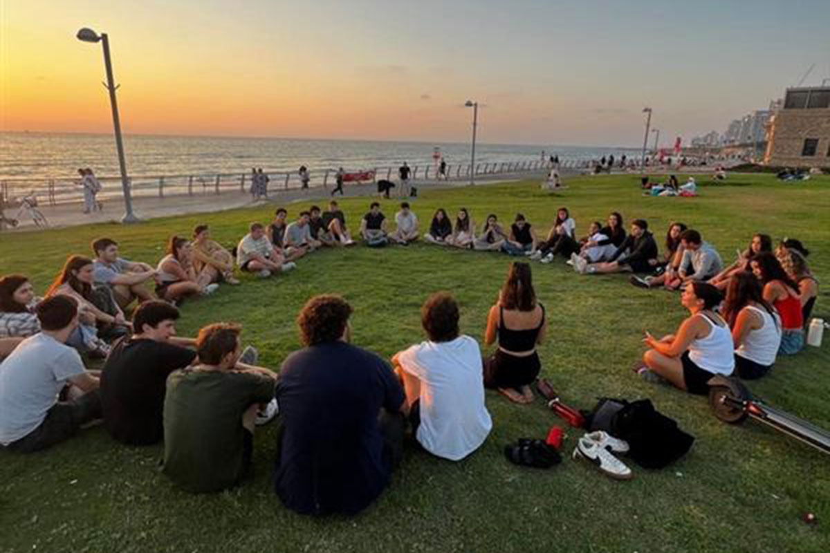A group of college students sitting in a circle on grass in Tel Aviv.