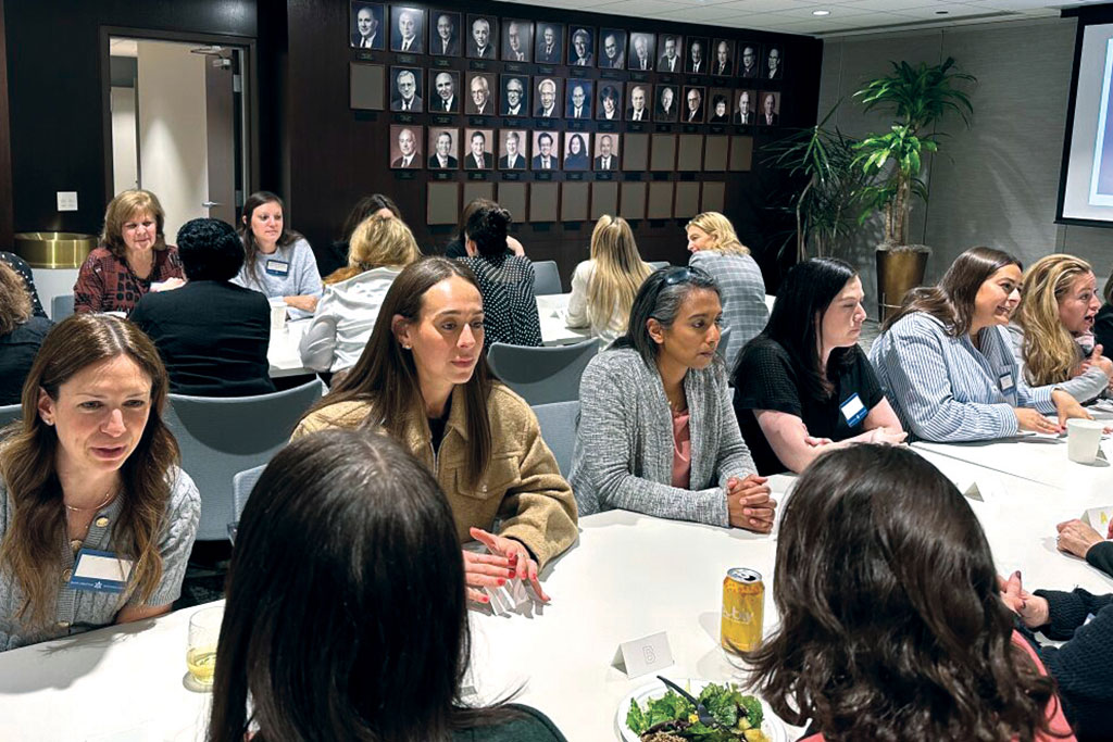 People seated around tables in a conference room participating in an event, with food and drinks on the tables.