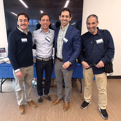 Four men in suits at a bagels and business networking event.