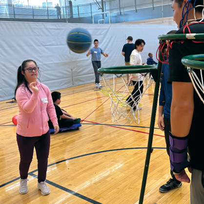 A child throwing a blue basketball in a hoop in a gym.